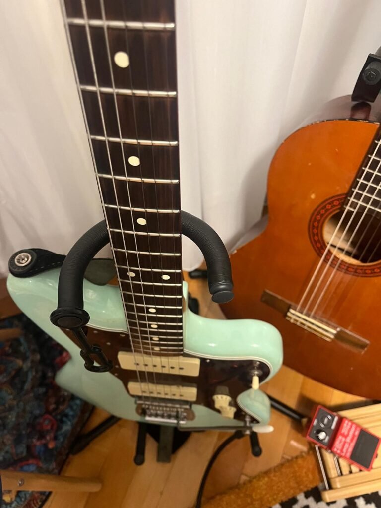Electric guitar with an acoustic guitar and effects pedal in the background, representing the range of gear covered in this guitar gear buying guide.